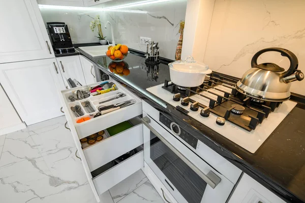 Interior de cozinha moderna branca luxuosa, gavetas puxadas para fora, porta de máquinas de lavar louça aberta — Fotografia de Stock