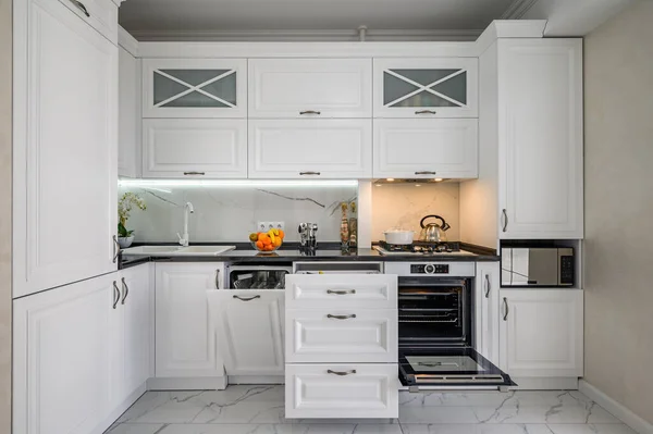 Luxusní bílý moderní kuchyňský interiér, vytažené zásuvky, otevřené dveře od myček nádobí — Stock fotografie
