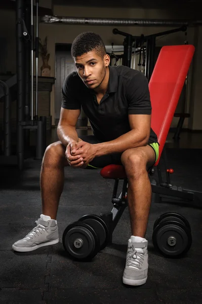 Młody człowiek siedzi na ławce w siłowni — Zdjęcie stockowe