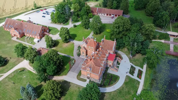 Jaunmoku Brick Medieval Castle Near Tukums, Latvia  at Pond With Fontain in Clear Sunny Summer Day From Above Top View. The Jaunmokas Manor Park. Aerial Dron 4k Shot