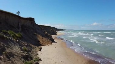 Kıyı şeridi üzerinde uçan Baltık Denizi Uçurumları Pavilosta Letonya 'nın yanındaki Kayalıklar ve Büyük Dalgalı Mağara Uçurumu ve Çakıl Taşları. Aerial Dron Manzarası. Kamera Geriye 4K Videosu Taşıdı