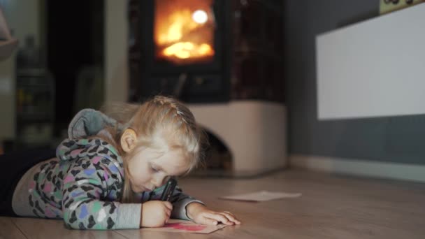 바닥에 소녀가 책쓰기와 그림그리기를 있습니다 배경에 불타는 난로가 분위기 — 비디오
