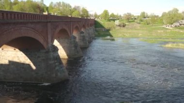 Uzun Eski Tuğla Köprüsü, Kuldiga, Letonya Venta Nehri 'nin karşısında. 4K Stedycam Dolly Shot. Avrupa 'nın En Geniş Şelalesi
