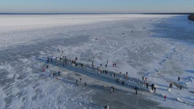 Buz kaplı eski ahşap iskelede donmuş Baltık Denizi 'nin ve güneşli bir kış gününde buzda yürüyen insanların Letonya' nın 4K seyahat sahnesinin keyfini çıkardığı video.