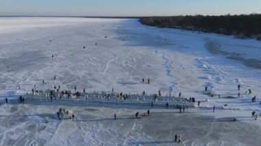 Buz kaplı eski ahşap iskelede donmuş Baltık Denizi 'nin ve güneşli bir kış gününde buzda yürüyen insanların Letonya' nın 4K seyahat sahnesinin keyfini çıkardığı video.