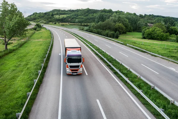 Big transportation truck on an Asphalt highway road or highway closeup against the background of rural landscape with green fields and forest on the horizon of blue sky