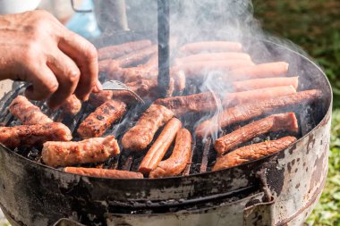 Bahçede ya da arka bahçede kömürlü barbekü ızgarası. Çok dumanlı ızgara sosis. Açık hava ızgarası için taşınabilir barbekü ızgarası