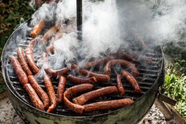 Bahçede ya da arka bahçede kömürlü barbekü ızgarası. Çok dumanlı ızgara sosis. Açık hava ızgarası için taşınabilir barbekü ızgarası