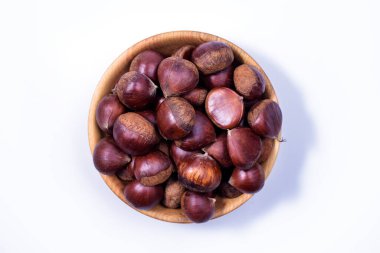 Beyaz arka planda tahta bir kasede kestaneler. Castanea sativa, tatlı olgun kestaneler, üst manzara