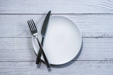 Boş beyaz bir tabakta çatal ve bıçak, beyaz ahşap masa arka planı.