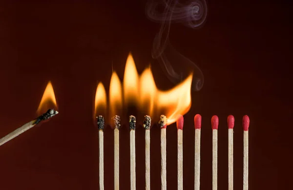Lit match next to a row of lighting matches. Red phosphorus matches on dark red background. Concept of ignition or initiation