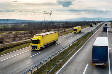 Parlak mavi bir günde bir otobanda geçen nakliye kamyonu konvoyu ya da kervanı. Beyaz ve kırmızı kamyonlu otoyol ulaşımı