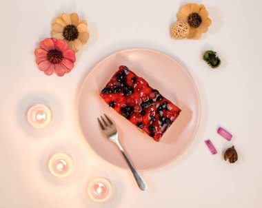 Pembe tabakta ahududu ve frenk üzümü soslu dilimlenmiş cheesecake, romantik mumlar, yakın görüş. Cheesecake 'in üzerine meyve sosu döküldü.