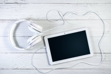 Tablet bilgisayar ve kulaklıklar beyaz ahşap yüzeyde. Müzik tableti modeli. Ekran kopyalama alanı için yol kırpılıyor
