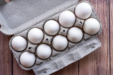 Tahta bir masanın üzerinde on beyaz yumurta bulunan bir karton yumurta kutusu. Kutudaki yumurtalar - Üst Görünüm