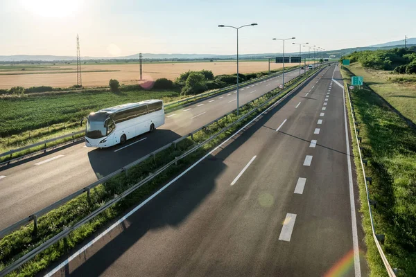 Modern White otobüsü kırsal bir zeminde geniş bir otoyolda seyahat ediyor. Yolcuların otobüs hattında karayolu taşımacılığı.