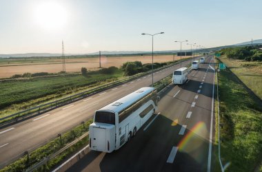 Kırsal bir zeminde geniş bir otoyoldan ayrılan modern beyaz otobüsler serisi. Otobüs konvoyu. Yolcuların otobüs hattında karayolu taşımacılığı.