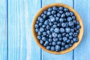 Eski mavi ahşap bir masada ahşap bir kasede taze yaban mersini. Sağlıklı ve diyet gıda konsepti. Yabanmersini antioksidandır. Üst Görünüm