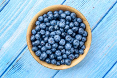 Eski mavi ahşap bir masada ahşap bir kasede taze yaban mersini. Sağlıklı ve diyet gıda konsepti. Yabanmersini antioksidandır. Üst Görünüm