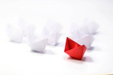 Liderlik kavramı. Beyazlar arasında öncülük eden kırmızı kağıt bir gemi. Kağıt beyaz gemiler kırmızı lider gemisinin gerisinde yüzüyor, seçici odaklanma.