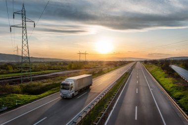Karavanı otoyolda, kargo taşımacılığı konsepti ilkbaharda - kargo servisi, arkasında dramatik bir günbatımı gökyüzü