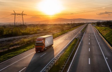 Gün batımında otoyolda elinde konteynır olan kırmızı bir kamyon. İlkbaharda kargo taşıma konsepti - kargo hizmeti, arka planda dramatik bir günbatımı gökyüzü