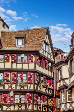 Colmar 'da büyüleyici dar bir caddede çiçek ve kepenkleri olan parlak tarihi kereste evleri..