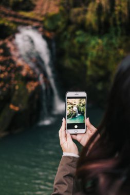 Kadın akıllı telefonuyla şelalenin fotoğrafını çekiyor. 