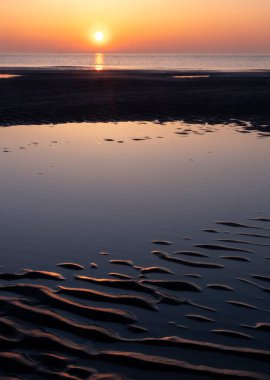 Kumsalda gün batımında güneşin suya batışının renkli yansıması.