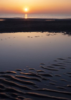 Kumsalda gün batımında güneşin suya batışının renkli yansıması.