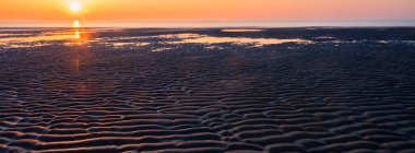 Kumsalda gün batımında güneşin suya batışının renkli yansıması.