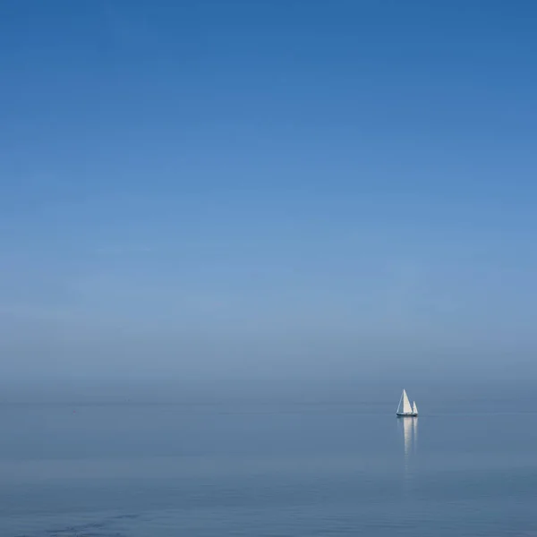 蓝天下广阔空旷湖中的蓝水上孤零零的帆船 — 图库照片