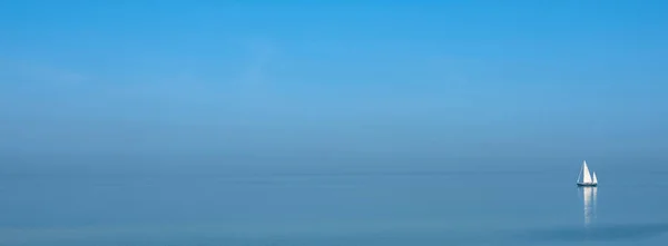 蓝天下广阔空旷湖中的蓝水上孤零零的帆船 — 图库照片