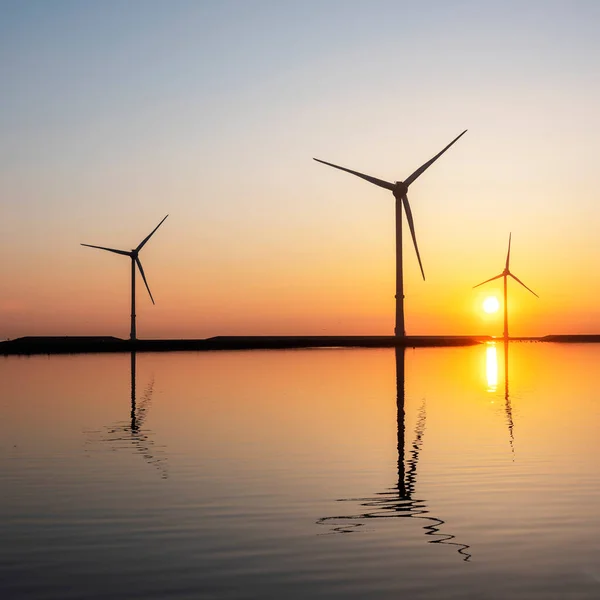 Wind turbines and colorful sunrise reflected in water — Stock Photo, Image