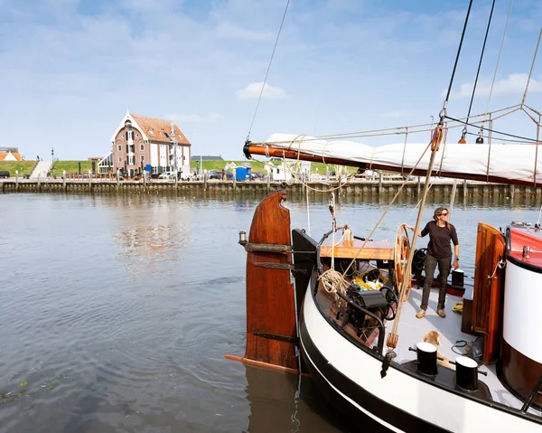 Woman steers old wooden sailing vessel in port of oudeschild on dutch island of texel while people fish for crab and man takes photograph — Stock Photo, Image