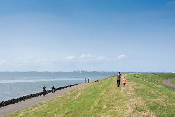 Mensen lopen en fietsen op dijk bij oudeschild op het Nederlandse eiland texel onder de blauwe hemel in de zomer — Stockfoto