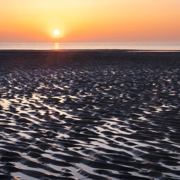 Patrón en arena y reflejo colorido de la puesta de sol en el agua — Foto de Stock