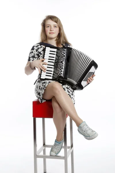 Teenage girl sits on red stool in studio with accordion — Stock Photo, Image