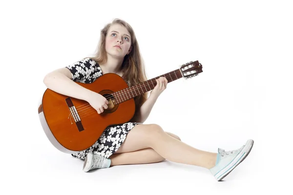 Usmívající se dospívající dívka v šatech hraje kytaru, sedí na fl — Stock fotografie