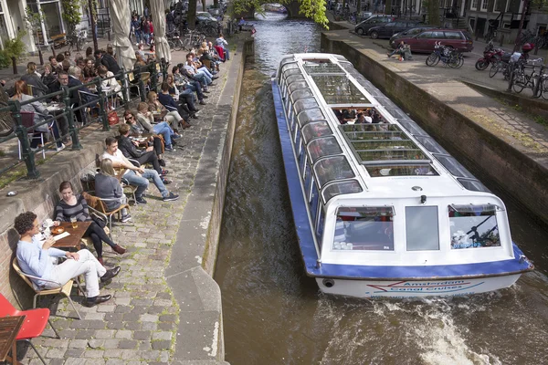 La gente disfruta de bebidas en el terraplén del canal de Amsterdam mientras touri — Foto de Stock