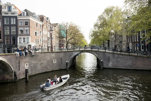 Young people sit on bridge over amsterdam canal while small boat — Stock Photo, Image