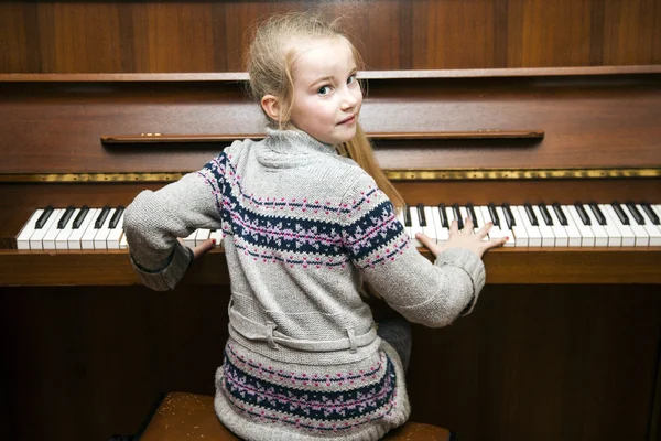 Jovem menina senta-se no marrom vertical piano — Fotografia de Stock