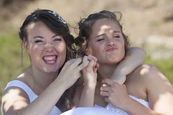 Dos novias sonríen y se divierten con sus anillos de bodas en la naturaleza —  Fotos de Stock