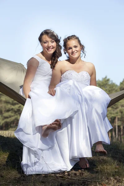 Duas noivas em rede contra o céu azul com fundo florestal — Fotografia de Stock