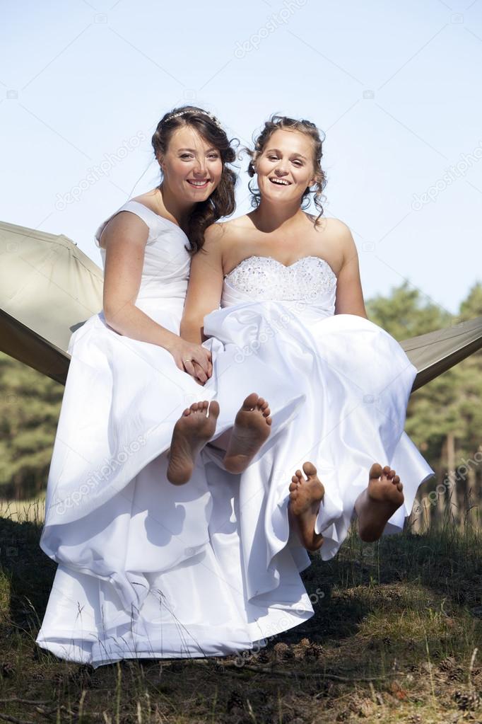 two brides in hammock against blue sky with forest background