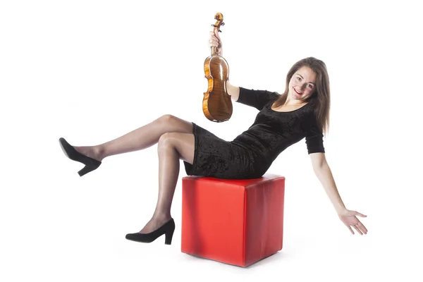 Brunette with violin has fun on red stool in studio — 스톡 사진