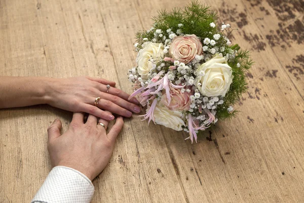 Hands of bride and groom with wedding ring on wooden table with — Stock Photo, Image