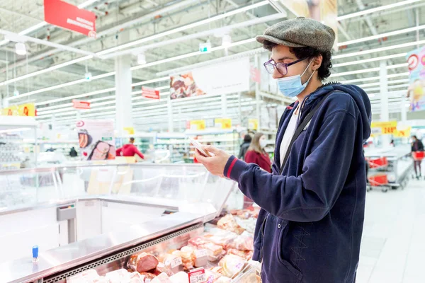 Jovem Com Uma Máscara Médica Examina Uma Variedade Salsichas Supermercado — Fotografia de Stock