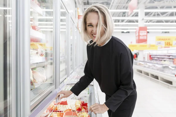 Laughing young woman in the frozen food department in a large light supermarket.