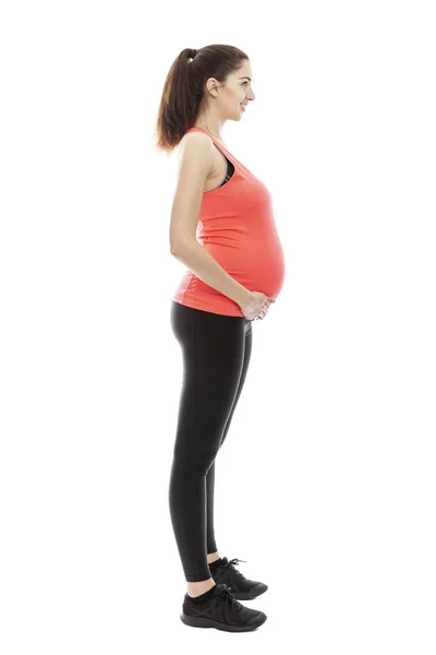 一个穿着运动服的孕妇正站在一个完全成长的时尚 配置文件视图 被白色背景隔离 垂直方向 — 图库照片